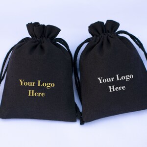 May include: Two black drawstring bags with the text "Your Logo Here" printed on them in gold and silver.