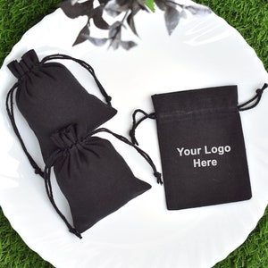 May include: Two black drawstring bags on a white plate. One bag has the text "Your Logo Here" printed on it.