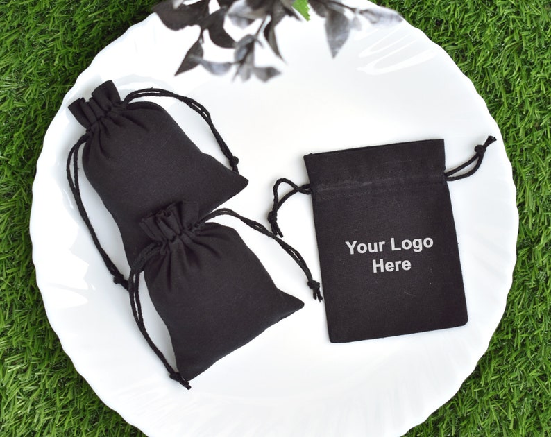May include: Two black drawstring bags on a white plate. One bag has the text "Your Logo Here" printed on it.