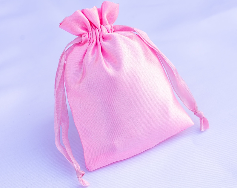 May include: A pink satin drawstring bag with a gathered top and long ties. The bag is empty and ready to be filled with a gift or small items.