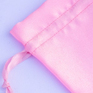 May include: A pink satin drawstring bag with a white cord. The bag is made of soft, silky fabric and has a smooth, shiny finish.