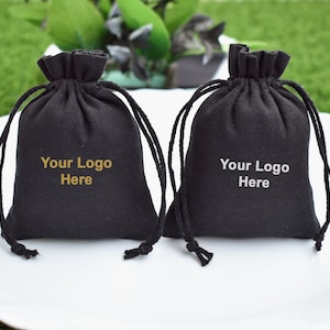 May include: Two black drawstring bags with a gold inscription that reads "Your Logo Here".
