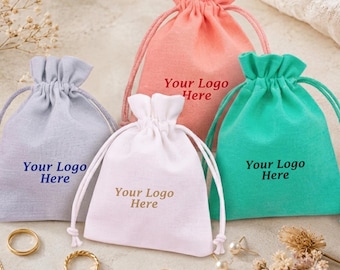 May include: Four small drawstring pouches in light gray, peach, white, and bright green. Each pouch features the text Your Logo Here printed on the front. The pouches are made of a soft fabric and include matching drawstrings to close the top.