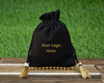 Könnte beinhalten: Schwarze Kordelzugtasche mit goldenen Verzierungen und Quasten. Die Tasche hat eine goldene Aufschrift mit dem Text "Your Logo Here".