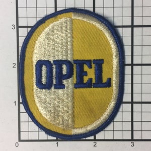 Könnte beinhalten: Ein blauer und gelber ovaler gestickter Aufnäher mit dem Wort "OPEL" in blauen Buchstaben.