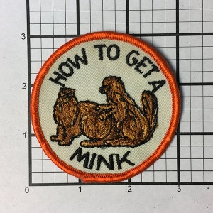 May include: A round, orange-bordered patch with a white background. The patch features a cartoon image of two brown minks with the text "HOW TO GET A MINK" in black.