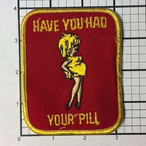 May include: A red embroidered patch with a yellow border. The patch features a cartoon woman in a yellow dress and the text "Have you had your pill?"