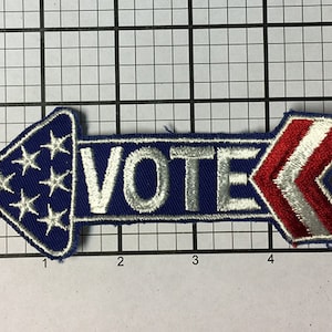 May include: A blue and red arrow-shaped patch with white stars and stripes. The word "VOTE" is embroidered in white on the patch.