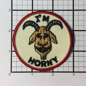 May include: A white embroidered patch with a red border. The patch features a cartoon goat with horns and the text "I'M HORNY".