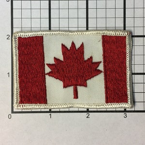 May include: A red and white embroidered Canadian flag patch with a white border.
