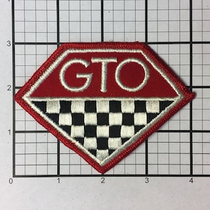 May include: A red diamond-shaped patch with white embroidered lettering that reads "GTO". The bottom half of the patch features a black and white checkered pattern.