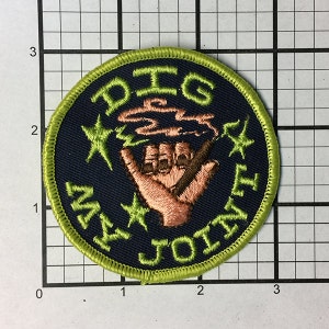 May include: A green and black embroidered patch with the text "DIG MY JOINT" and a hand holding a joint with smoke coming from it.