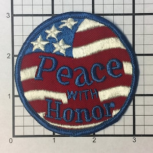 May include: A round, blue, white, and red embroidered patch with an American flag design. The text "Peace with Honor" is embroidered in blue on the patch.