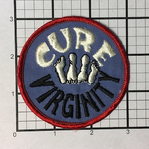 May include: A blue and red embroidered patch with the words "Cure Virginity" in white and black lettering. The patch features a graphic of three white feet.
