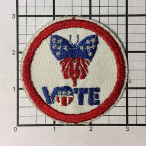 Może przedstawiać: Naszywka haftowana w kolorze czerwonym, białym i niebieskim z motylem i napisem "VOTE".