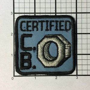 Könnte beinhalten: Ein blauer gestickter Aufnäher mit schwarzen Nähten. Der Aufnäher lautet "CERTIFIED C.B.O." mit einer silbernen gestickten Mutter und Schraube in der Mitte.