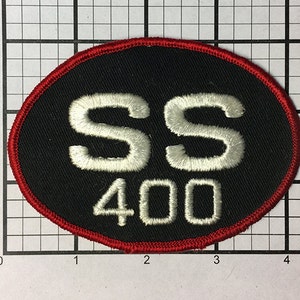 May include: A black oval patch with a red border. The patch has white embroidered text that reads "SS 400".