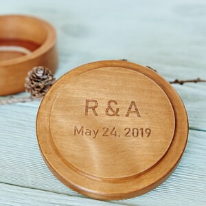 Pu&ograve; includere: Una scatola per anelli in legno con un coperchio inciso con le iniziali "R&A" e la data "May 24, 2019".
