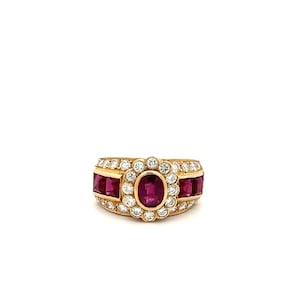 May include: A gold ring with a large oval ruby surrounded by smaller diamonds. The ring has three rows of smaller rubies on either side of the center stone.