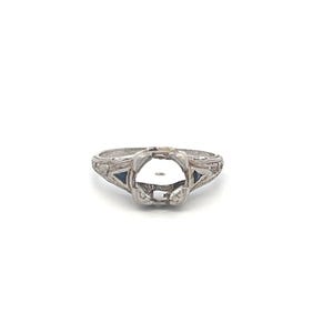May include: A silver ring with a filigree design and two small blue gemstones. The ring is designed to hold a larger center stone.