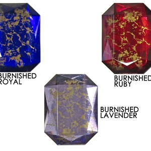 May include: Three glass cabochons with gold flecks. The cabochons are in the colors of blue, red, and purple. The text "Burnished Royal", "Burnished Ruby", and "Burnished Lavender" is below each cabochon.
