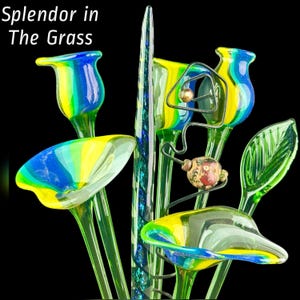 May include: A collection of glass art pieces featuring the text Splendor in The Grass. The arrangement includes blue and yellow striped trumpet-shaped flowers, a tall green spiraled spire, a green leaf, and a wire stem with a patterned bead.