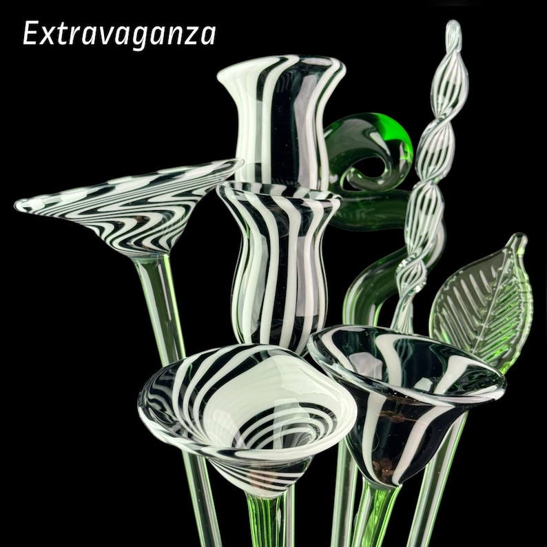 May include: A collection of glass sculptures featuring the word Extravaganza. The set includes trumpet-shaped flowers with black and white striped patterns, a green glass spiral, and a green glass leaf, all supported by thin green glass stems.