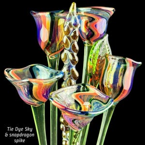 May include: A collection of hand-blown glass flowers featuring swirling tie-dye patterns in orange, blue, and purple hues, accompanied by a central textured glass snapdragon spike. The text Tie Dye Sky & snapdragon spike is visible.