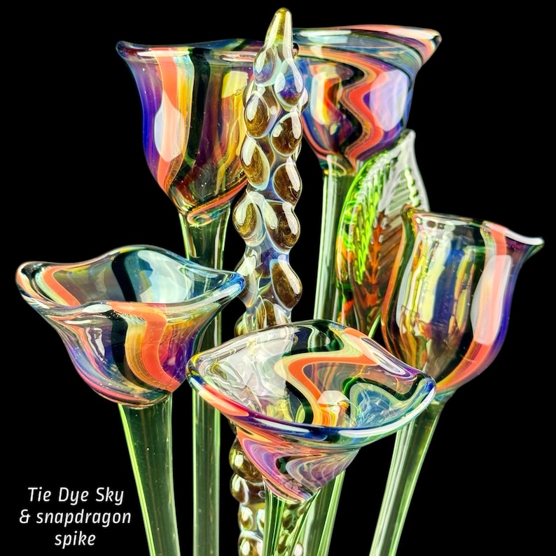 May include: A collection of hand-blown glass flowers featuring swirling tie-dye patterns in orange, blue, and purple hues, accompanied by a central textured glass snapdragon spike. The text Tie Dye Sky & snapdragon spike is visible.