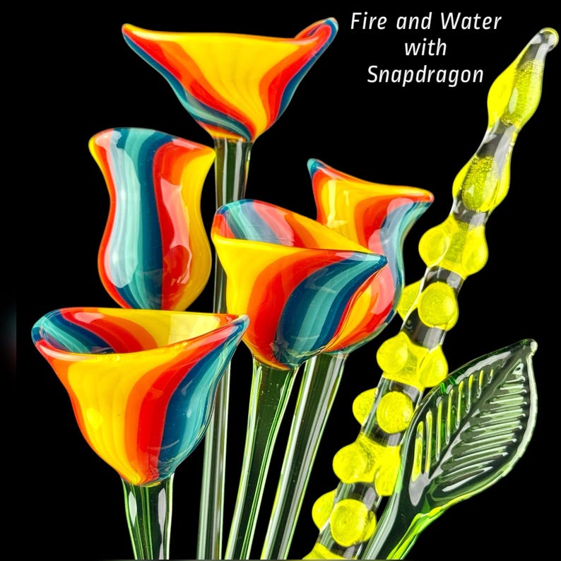 May include: A collection of glass sculptures featuring four trumpet-shaped flowers with swirling red, orange, yellow, and blue stripes, alongside a tall yellow textured stem with a green leaf. The text Fire and Water with Snapdragon is visible.