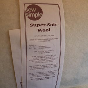 Può includere: Un'etichetta marrone con testo bianco che recita "sew simple Super-Soft Wool 100% Wool Wadding with Scrim Made with 100% Triple Washed New Zealand Slipe" e dettagli sulla ovatta di lana, tra cui le dimensioni, le istruzioni per la cura e il restringimento.