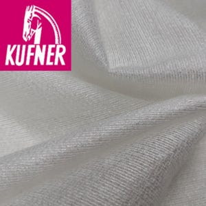 Può includere: Primo piano di tessuto bianco con trama strutturata. Il tessuto è piegato, mostrando l'interazione di luce e ombra. L'angolo in alto a sinistra presenta un rettangolo rosa con la scritta "KUFNER" e un logo a forma di testa di cavallo.