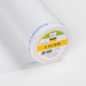 May include: A white roll of Vilene L 11/310 fusible interfacing. The label is yellow with black text and a red logo. The interfacing is 25% CV, 45% PES, 30% PA.
