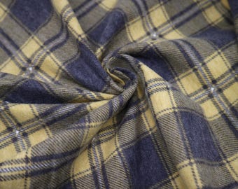 Puede incluir: Primer plano de una tela doblada con un patrón de cuadros. La tela presenta una combinación de amarillo mostaza, azul marino y tonos grises. Se ven pequeños adornos blancos dispersos.