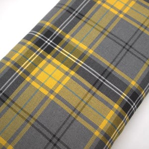 Op de afbeelding: Een gevouwen stuk stof met een klassiek tartan ruitpatroon. Het ontwerp bestaat uit elkaar kruisende horizontale en verticale lijnen in tinten antracietgrijs, felgeel en zwart, met dunne witte accentstrepen door het hele patroon.
