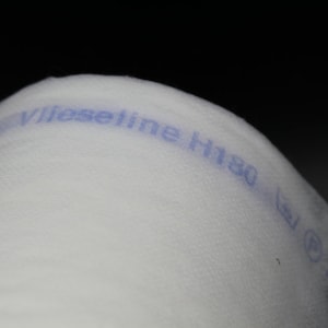 May include: Close-up of a roll of white fabric with the text "Vlieseline H180" printed in blue. The fabric appears to be a lightweight interfacing material, often used in sewing and crafting projects. The background is black.