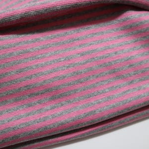 May include: A piece of fabric featuring a repeating pattern of horizontal stripes in alternating shades of heather gray and bright pink. The material has a visible knit texture with a soft, folded drape that creates subtle shadows across the surface.