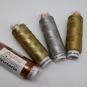 May include: Four spools of metallic thread in gold, silver, copper, and bronze. The spools are labeled "Barkonie Victoria" and have the thread weight and color number printed on them.