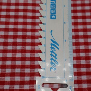 May include: A white and red gingham fabric with a ruler measuring 20 centimeters. The ruler is labeled "Mettler" and has markings in centimeters and inches.
