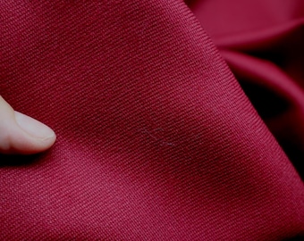 May include: Close-up of a deep red fabric with a subtle woven texture. The material is tightly woven, creating a smooth surface. The fabric is slightly folded, showing the depth and drape of the material. The colour is a rich, saturated shade of red.