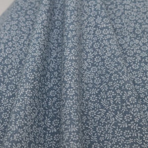 May include: A close-up of a blue fabric with a white floral pattern. The fabric has a subtle texture and a soft, slightly faded look.