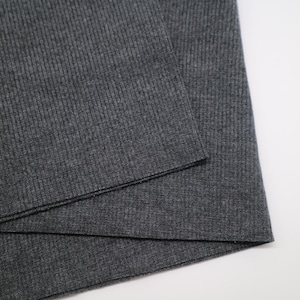 May include: A dark charcoal gray fabric featuring a fine vertical ribbed texture. The material is folded over itself, displaying a consistent knit pattern across the surface with a matte finish and a clean, straight edge along the fold line.