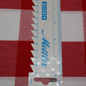 May include: A white ruler with blue markings and the word "Mettler" printed on it. The ruler is placed on top of a red and white checkered fabric.