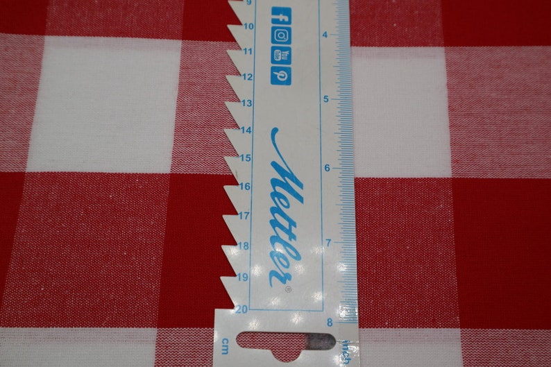 May include: A white ruler with blue markings and the word "Mettler" printed on it. The ruler is placed on top of a red and white checkered fabric.
