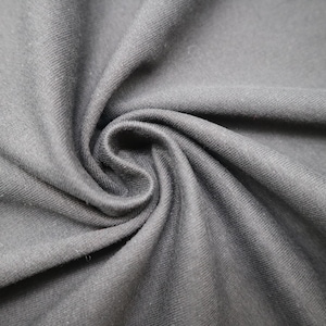 May include: A solid dark charcoal gray fabric with a visible diagonal twill weave texture. The material is gathered in the center, creating soft, flowing folds and deep shadows that highlight the matte finish and consistent color of the textile.