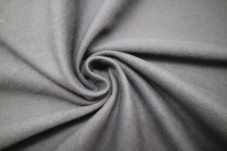 May include: A solid dark charcoal gray fabric with a visible diagonal twill weave texture. The material is gathered in the center, creating soft, flowing folds and deep shadows that highlight the matte finish and consistent color of the textile.