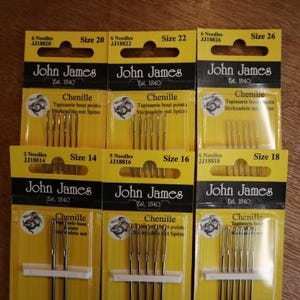 May include: Six packs of John James Chenille needles in sizes 14, 16, 18, 20, 22, and 26. Each yellow and black card features the brand name, needle count, and size. The needles are visible through clear plastic blisters on each card.