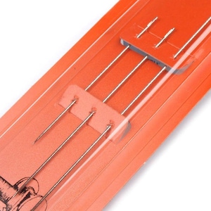 May include: A close-up of a package of four silver sewing needles on a bright orange background. The needles are packaged in a clear plastic sleeve.