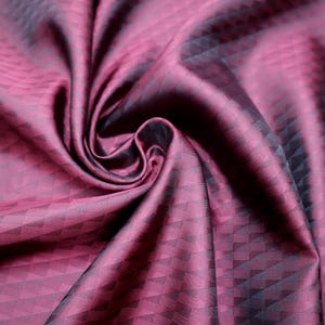 Puede incluir: Primer plano de una tela burdeos con un patrón geométrico. La tela está drapeada y doblada, creando sombras y reflejos. El patrón consiste en pequeños triángulos oscuros dispuestos en filas y columnas, dando una apariencia texturizada. La tela tiene un ligero brillo.