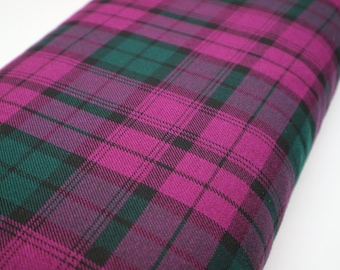 Puede incluir: Una pieza de tela con un vibrante patrón de cuadros con líneas que se cruzan en tonos magenta, verde bosque profundo y finas rayas negras. El tejido tiene una textura visible y está doblado para mostrar el diseño de tartán repetitivo.